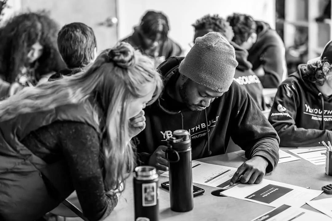 An instructor leans over a participant's worksheet during a group lesson.
