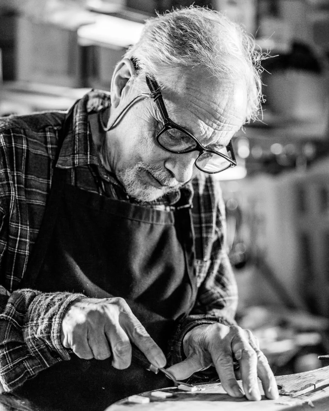 A craftsman shapes wood at a workbench in his instrument shop.