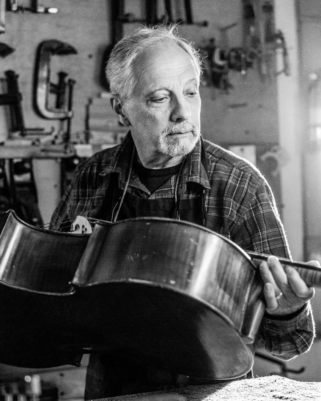 A man examines an unfinished acoustic guitar in his workshop.