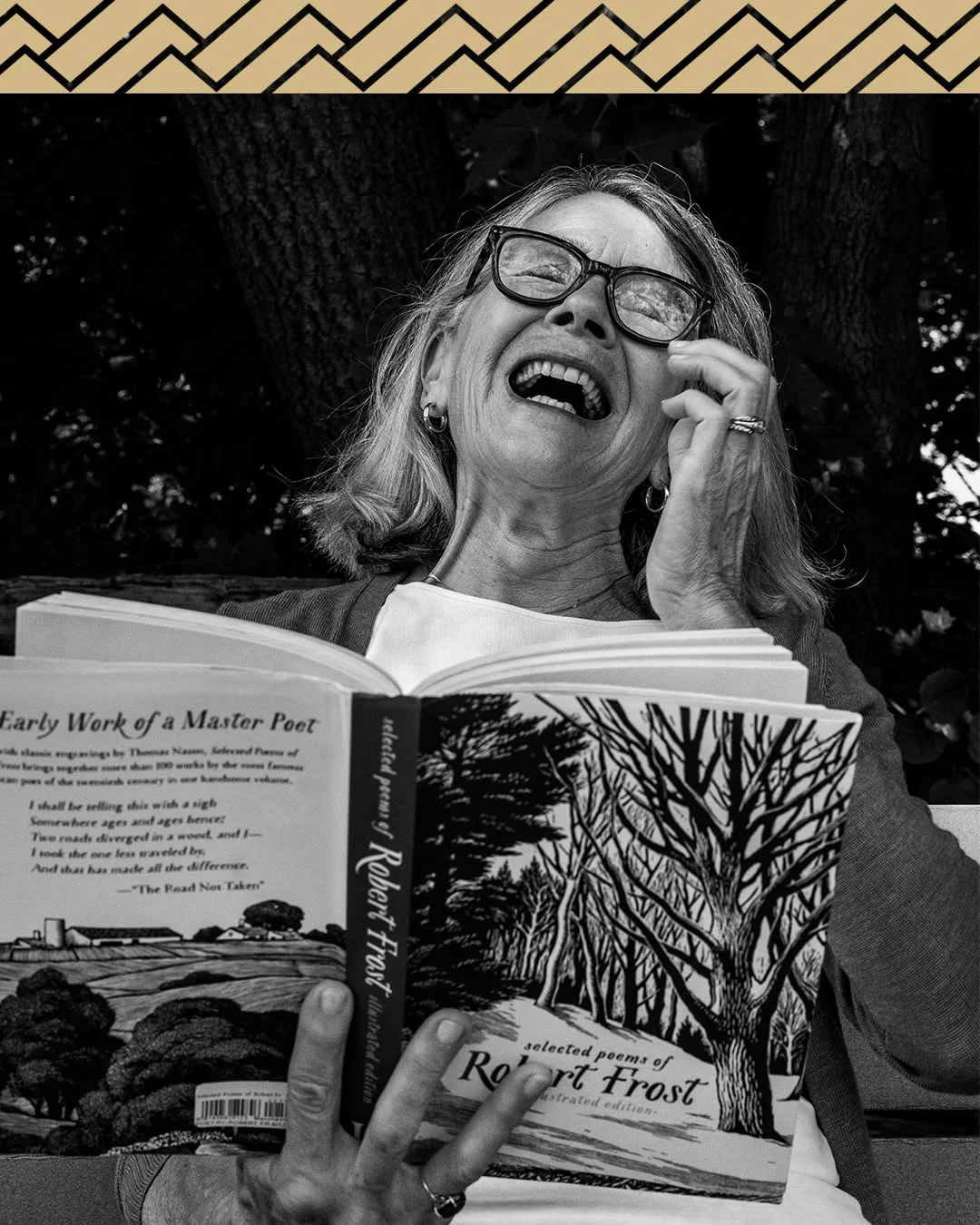 A woman laughs over an open book of Robert Frost poems.
