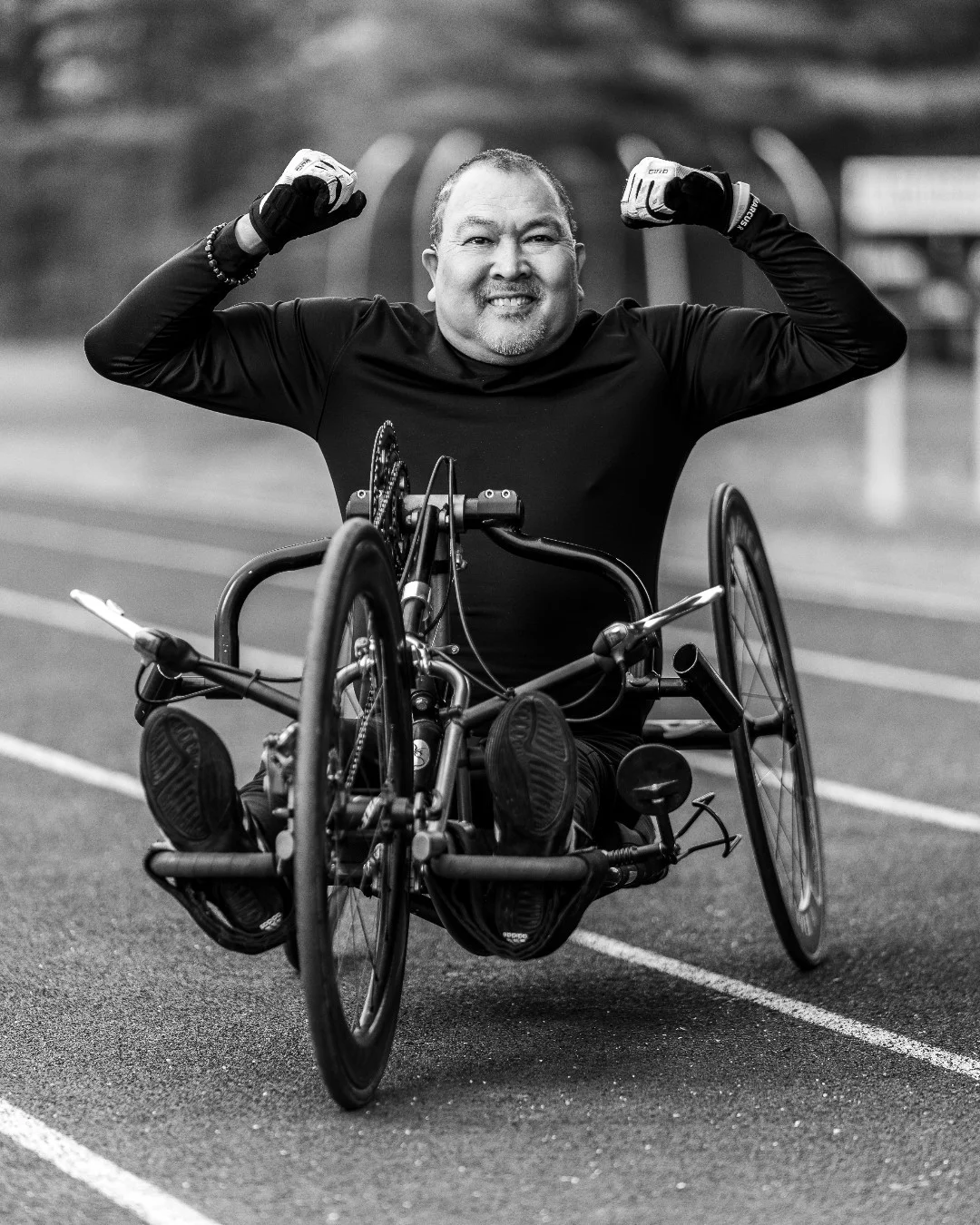 A handcyclist raises both fists while seated in his racing chair on a track.