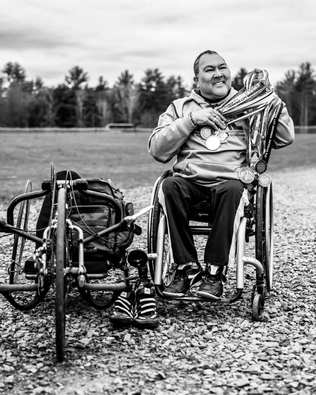 A handcyclist sits beside his cycle while holding his helmet.