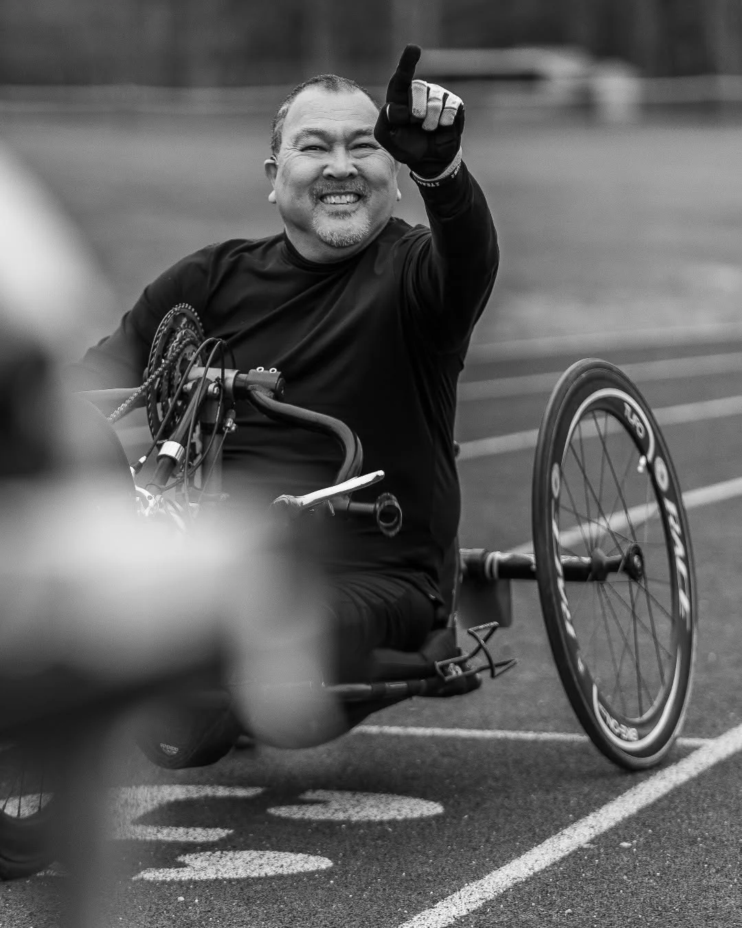 A handcyclist raises one fist while riding on an outdoor track.