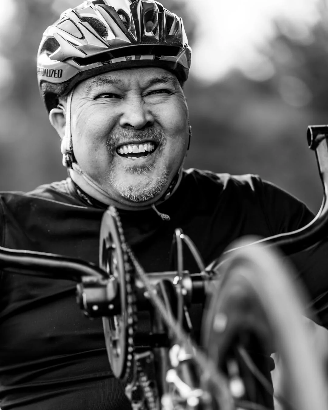 A smiling handcyclist wears a helmet during an outdoor ride.