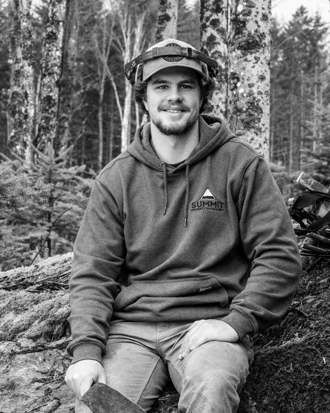 Ty Garon sits on a mossy stump at a wooded worksite.