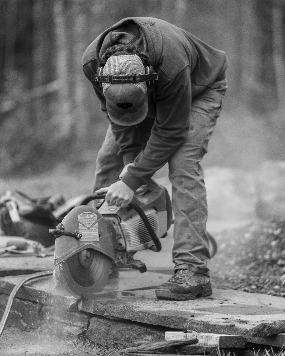 Ty Garon bends over a stone slab while cutting it with a masonry saw.