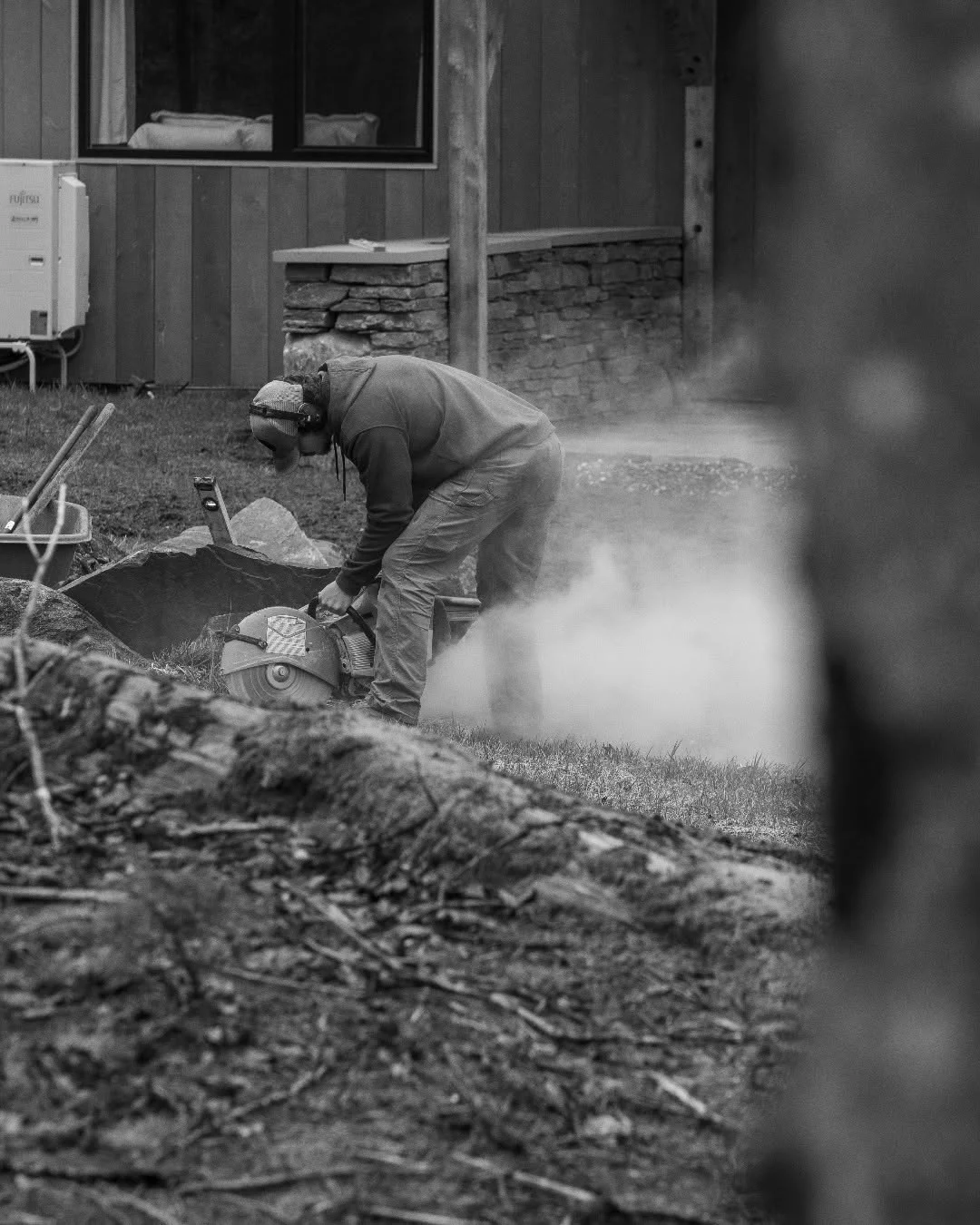 Ty Garon cuts stone near a house as dust rises around him.