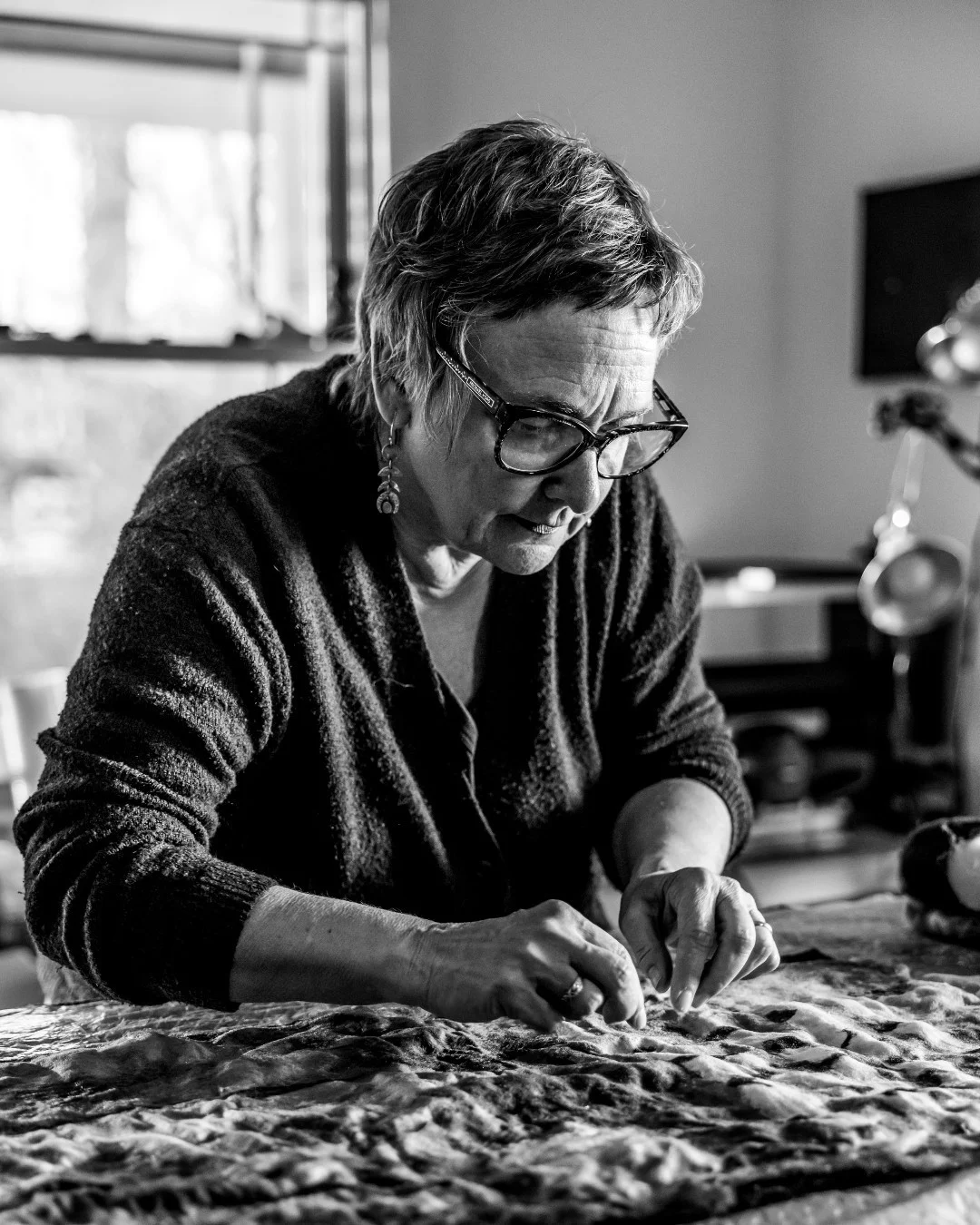 Susi Ryan presses loose fibers into a patterned felt panel on a worktable.