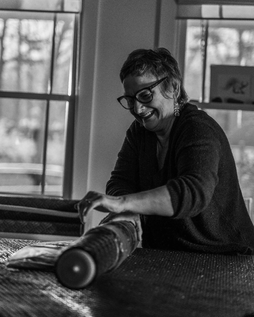 Susi Ryan smiles while rolling felt around a cylinder on her worktable.
