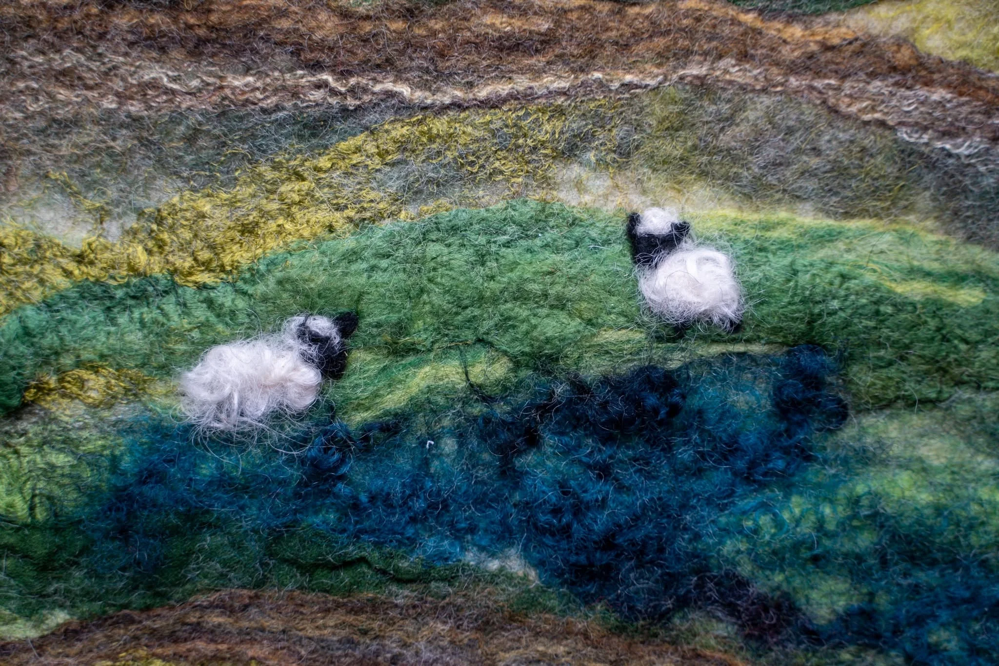 A colorful felt landscape shows two sheep beneath a rainbow sky.
