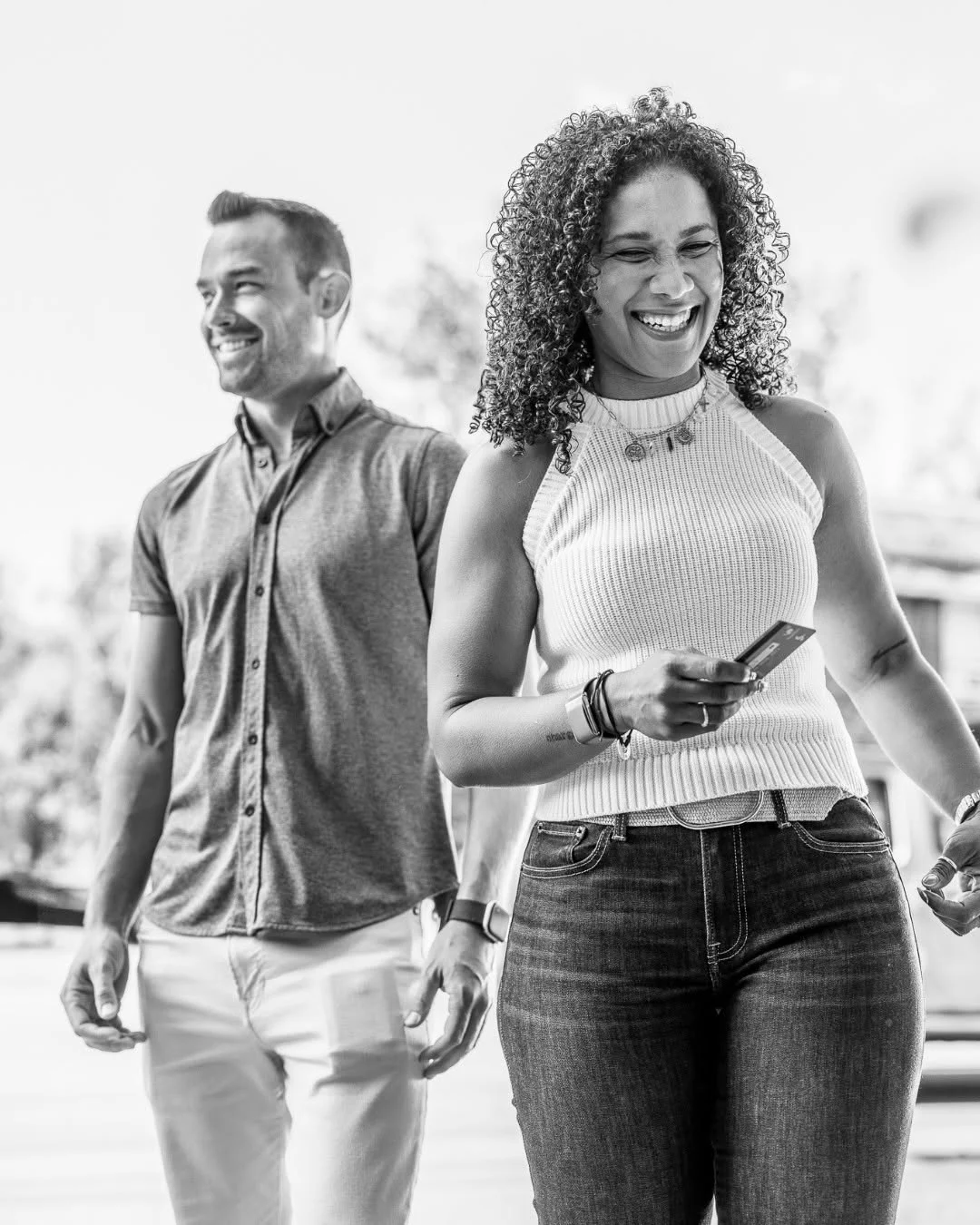 A smiling couple walks outdoors as the woman holds a bank card.
