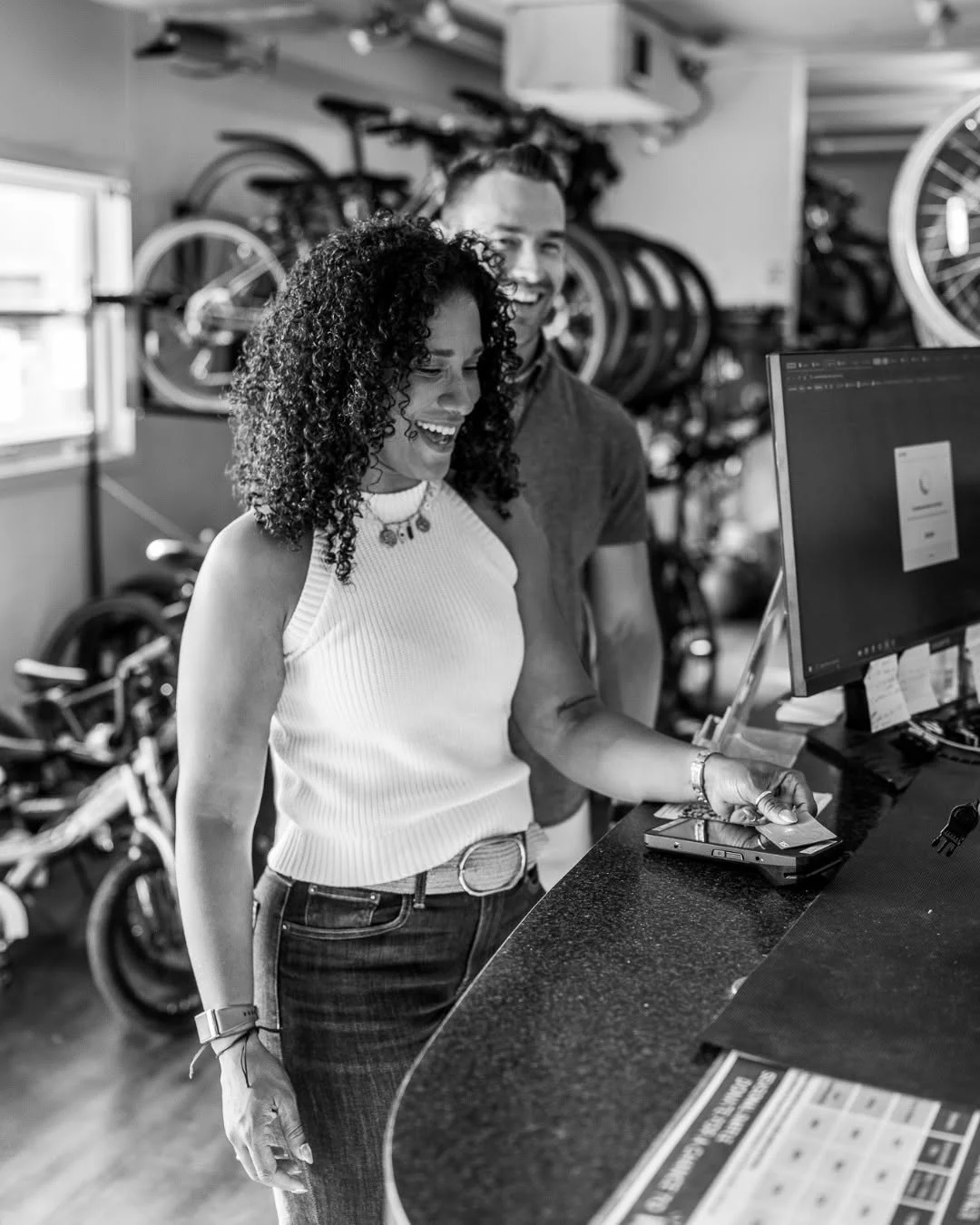 A woman smiles at a bike shop counter with bicycle wheels behind her.