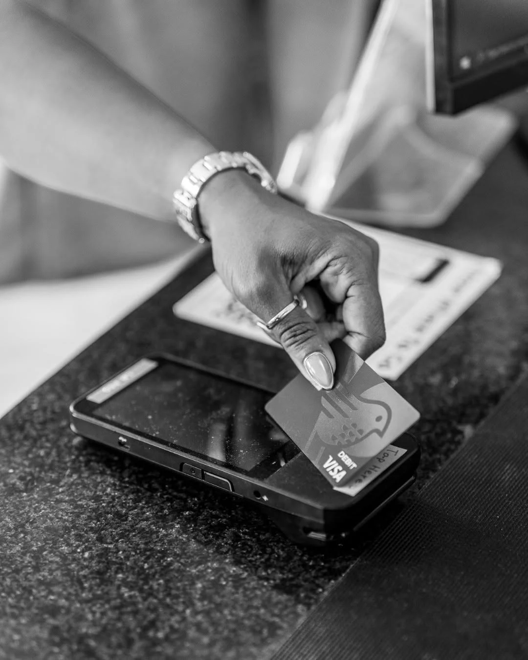 A hand taps a bank card against a countertop payment terminal.