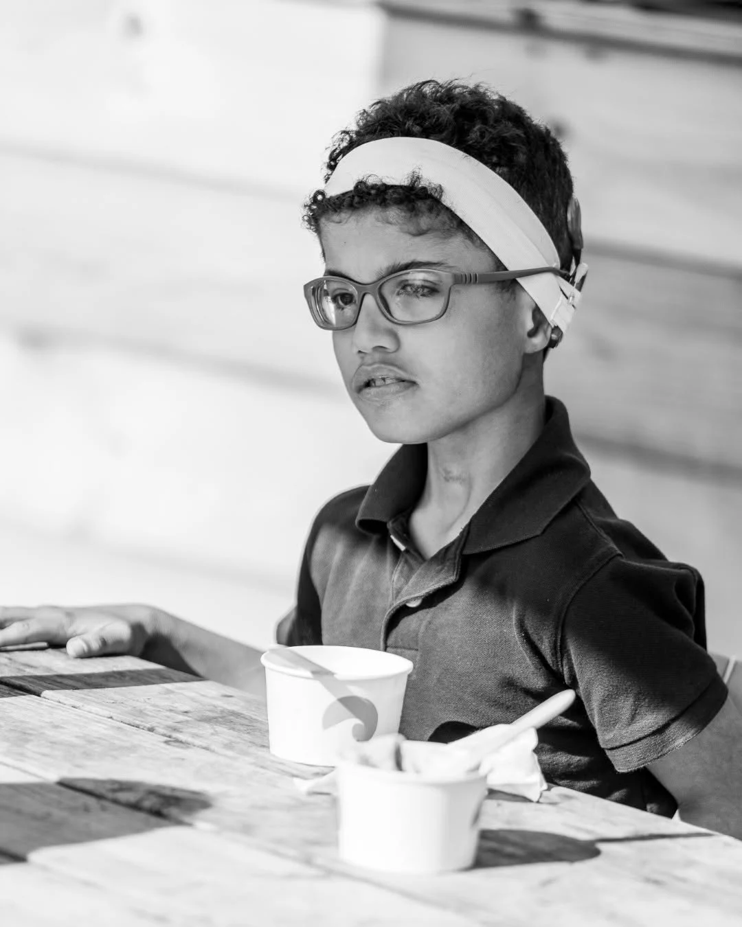 A boy wearing a headband sits at an outdoor table with paper cups.