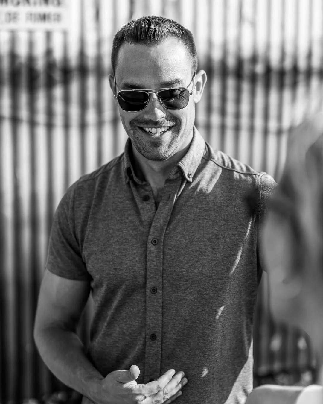 A smiling man wearing sunglasses stands outdoors.