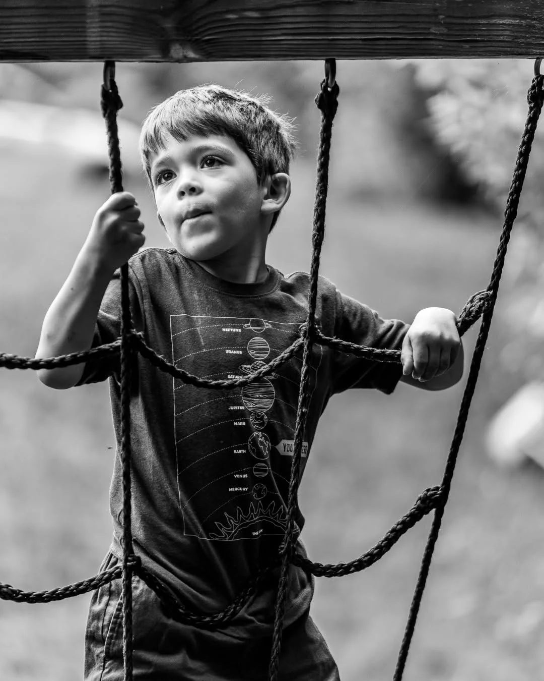 A young boy grips the ropes of a playground climbing net.