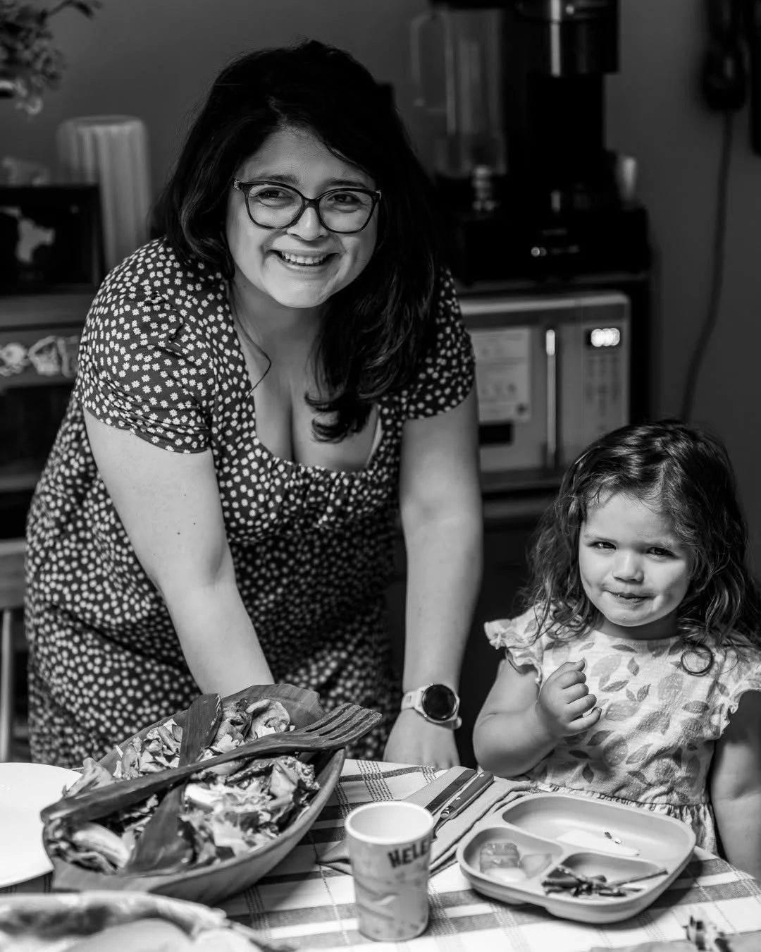 A woman and young girl smile beside plates of food at a dining table.