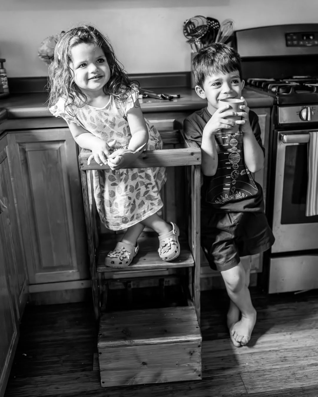Two children share a step stool in a kitchen.