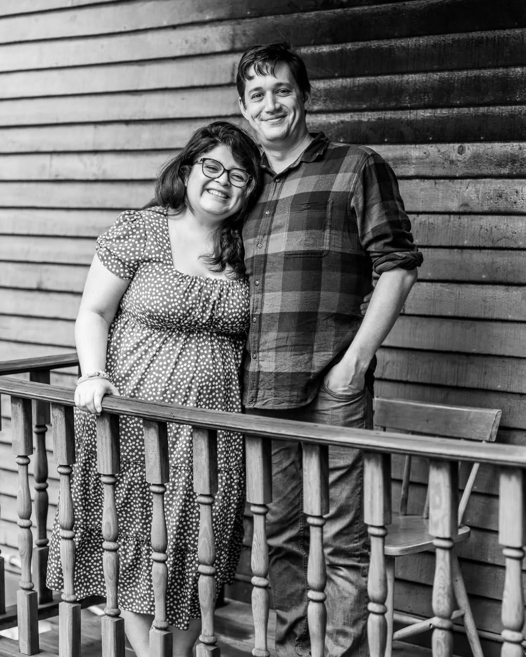 A couple stands together on a wooden porch.