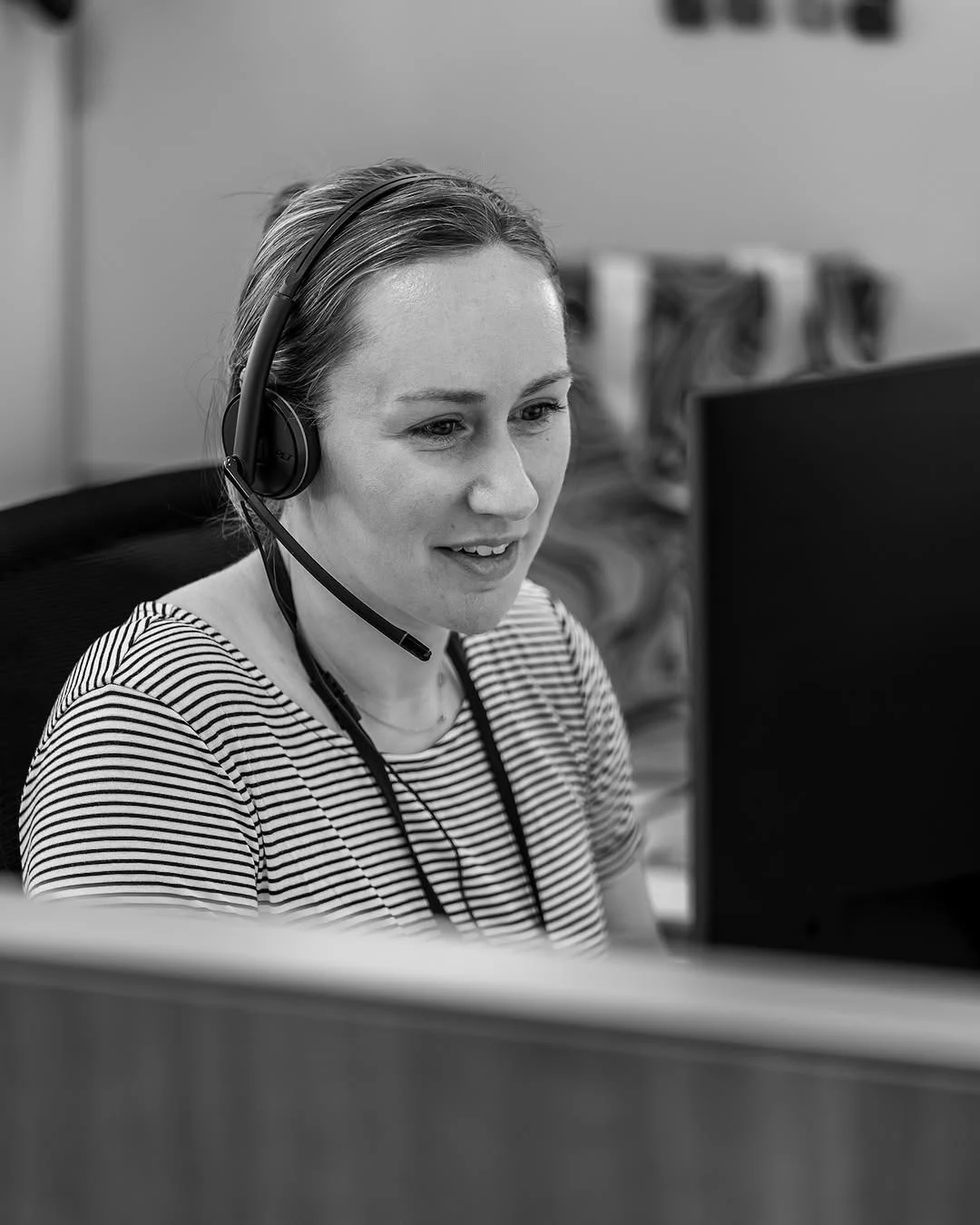A woman wearing a headset works at a computer.
