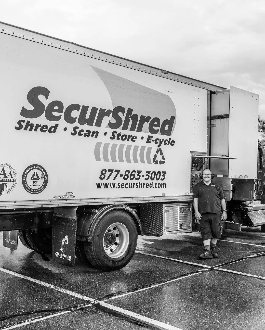A worker stands beside a SecureShred truck in a wet parking lot.