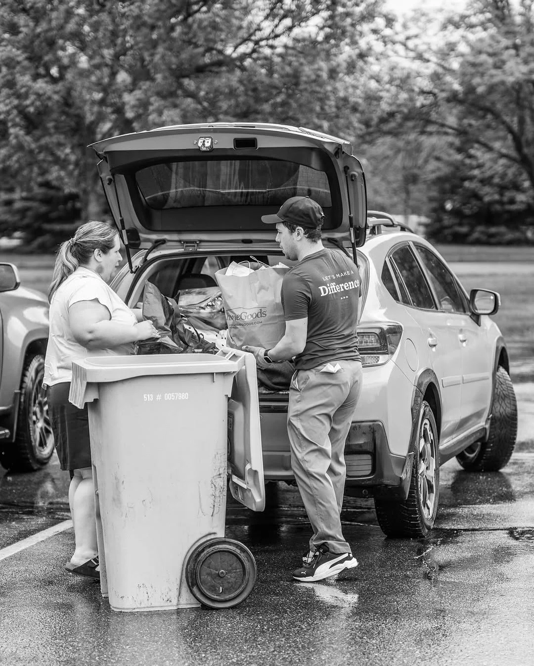 A worker helps an attendee load a wheeled document bin beside an open SUV.