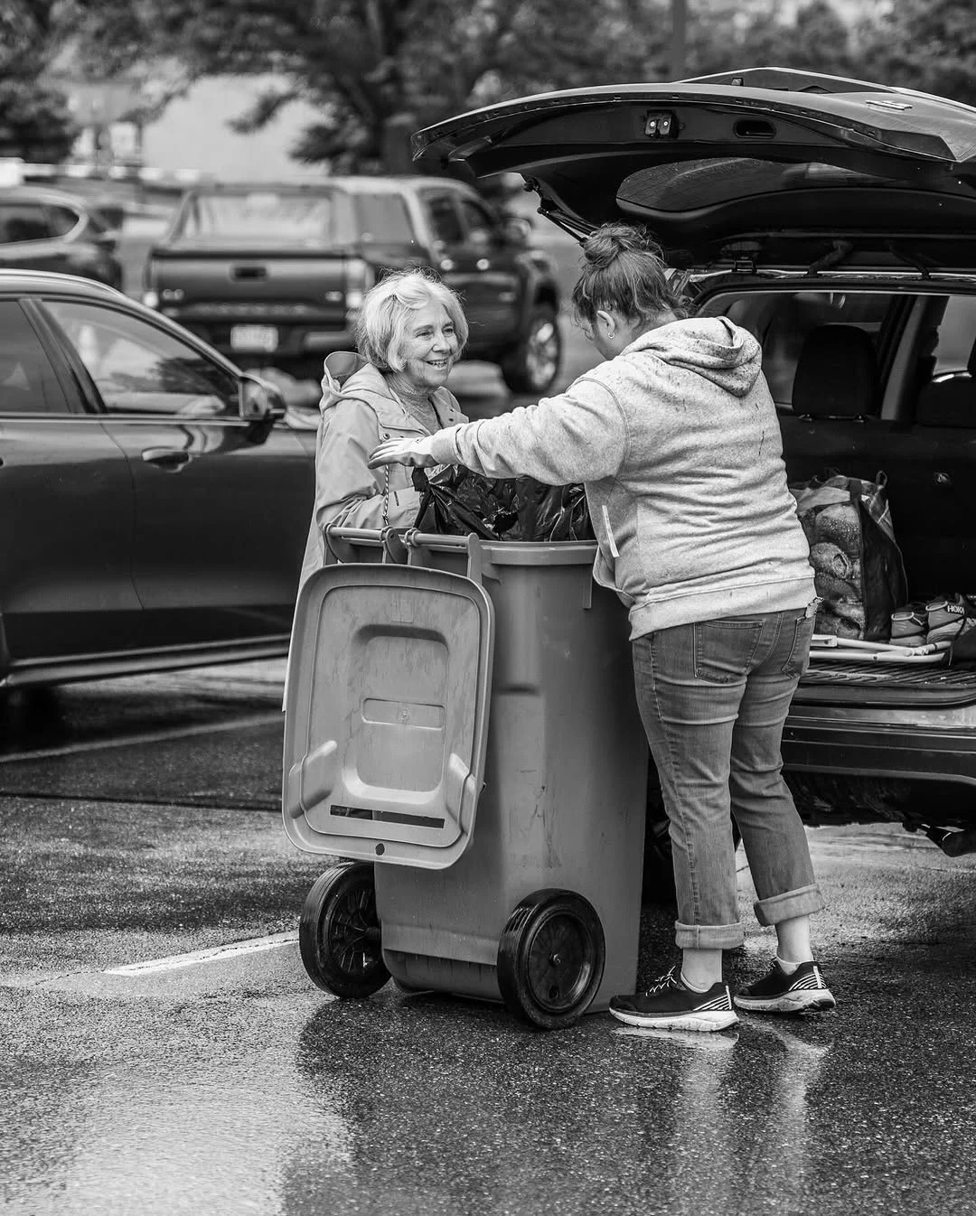 Two attendees push a wheeled document bin past an open car trunk.