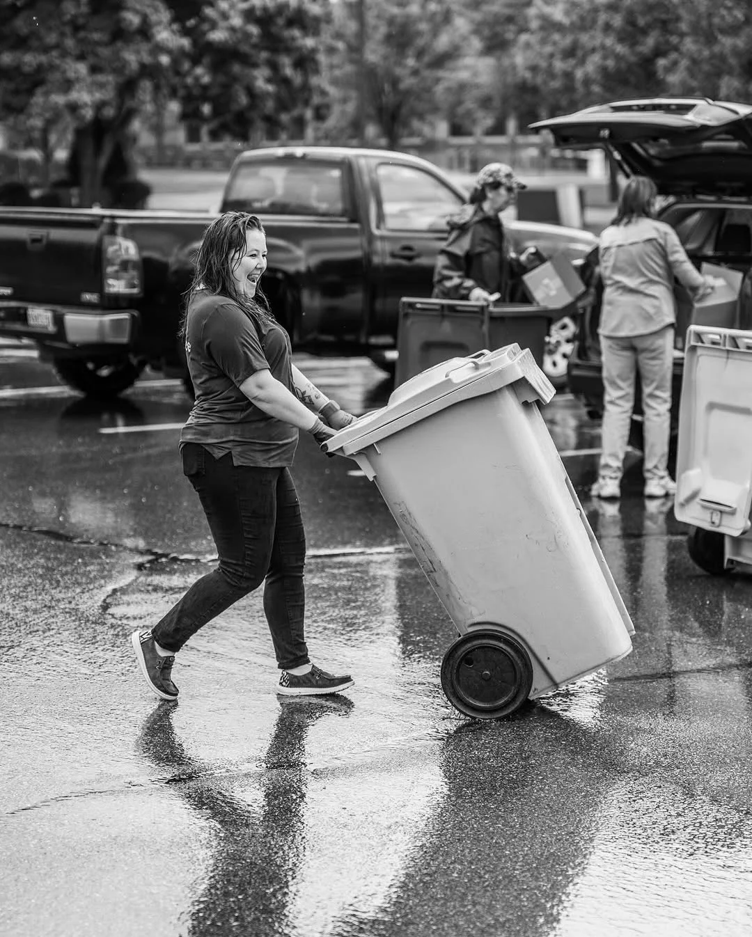 A worker rolls a document bin across a rain-soaked parking lot.