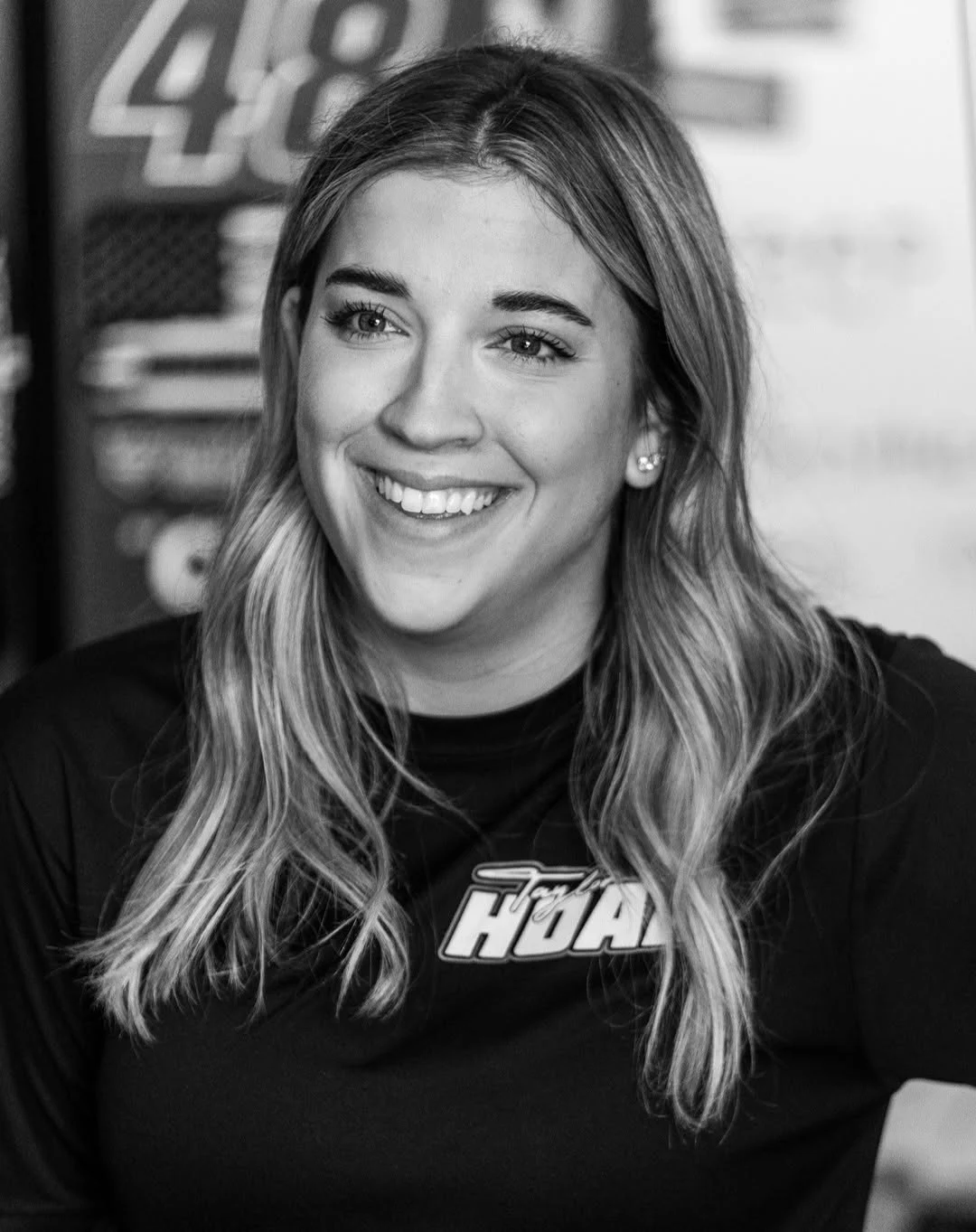 Black-and-white headshot of Taylor Hoar smiling in a Taylor Hoar Racing shirt.