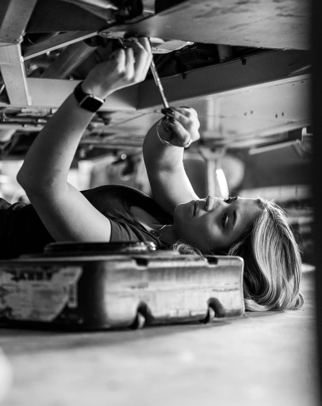 Taylor Hoar lies beneath a race car and works overhead with a hand tool.