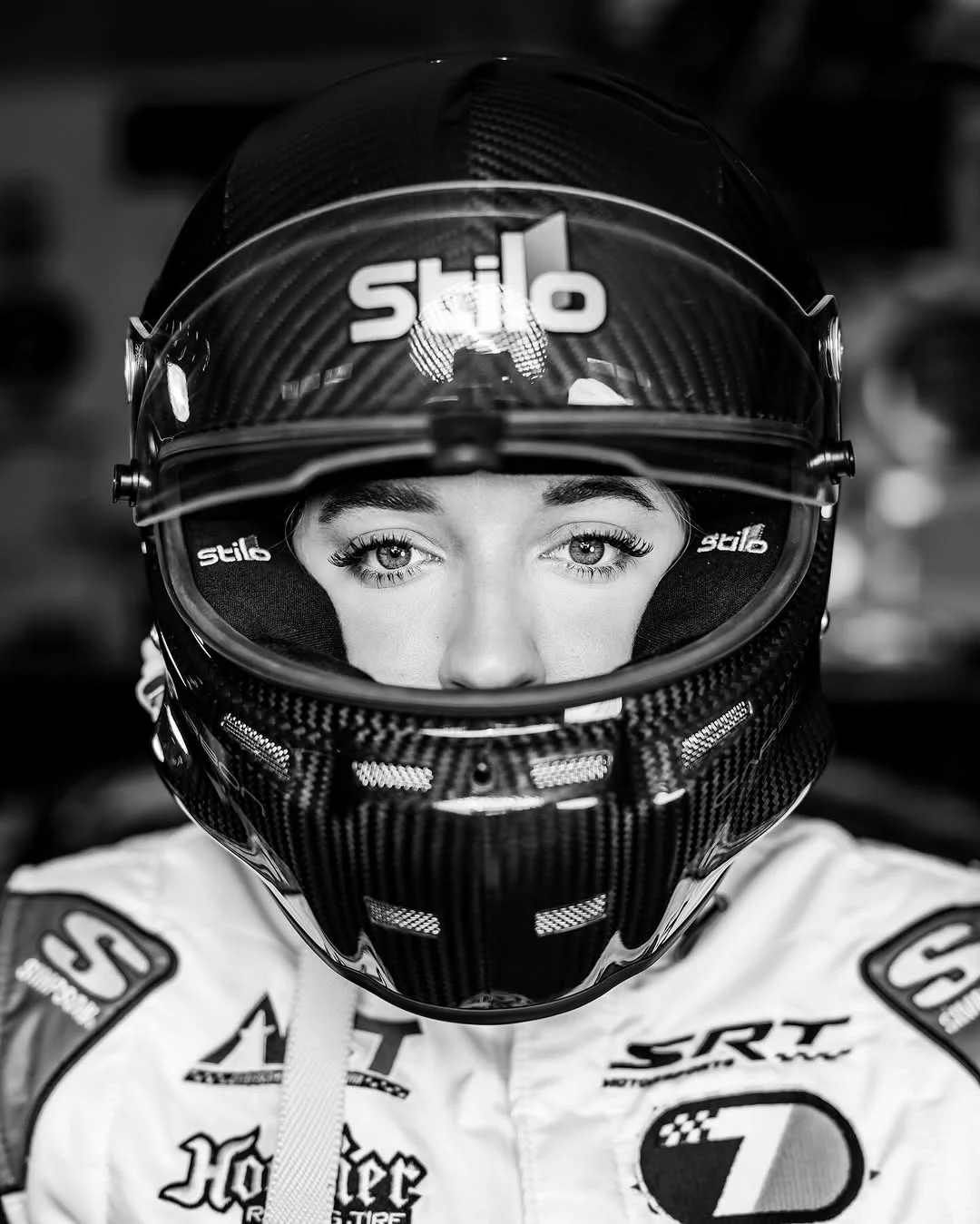 Black-and-white close portrait of Taylor Hoar looking through the visor of her racing helmet.