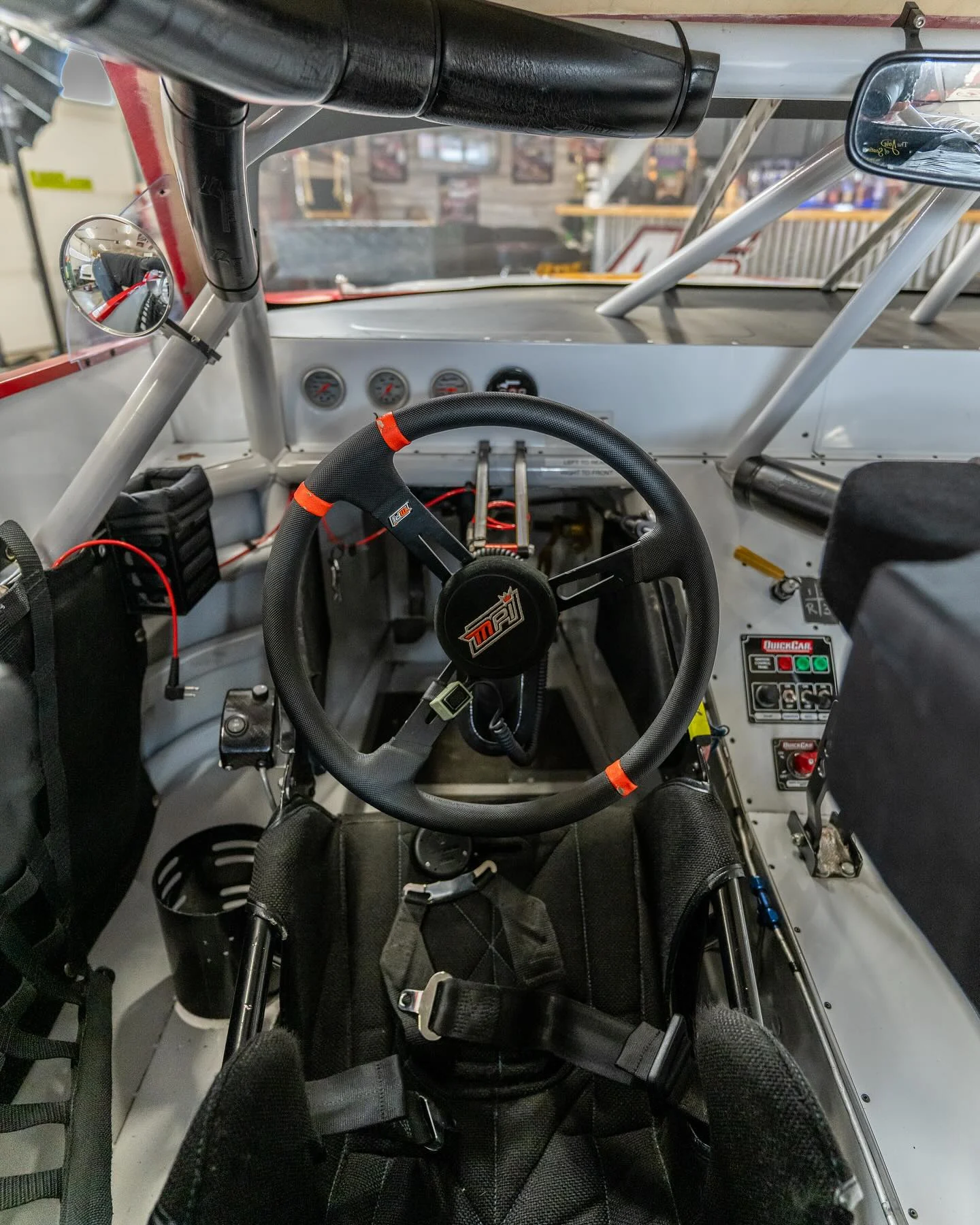 The driver’s seat, steering wheel, gauges, and roll cage inside a stock car.