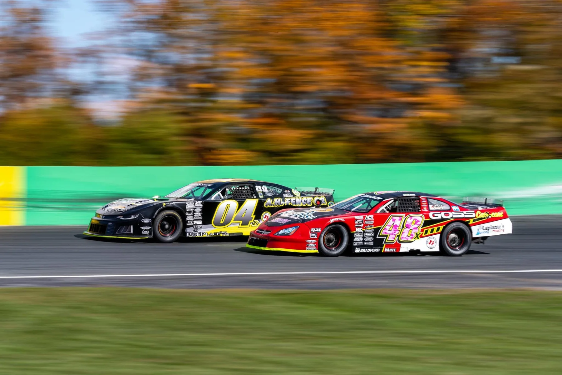 The black No. 04 and red No. 48x stock cars race side by side past the green wall.