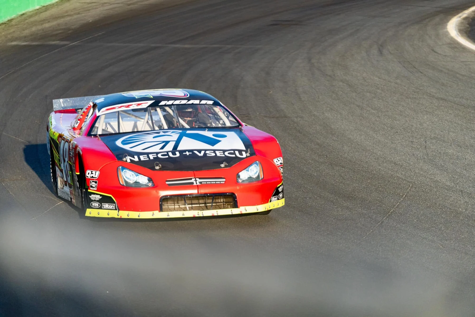 Head-on view of Taylor Hoar's red No. 48 car with a NEFCU + VSECU hood logo rounding a banked corner.