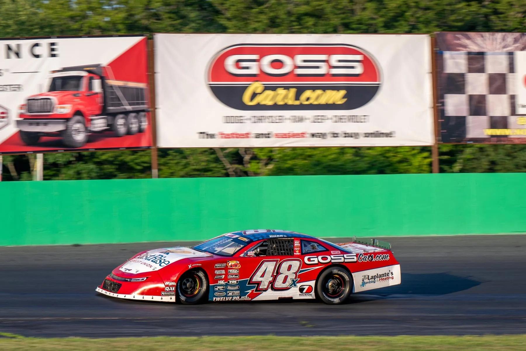 Taylor Hoar’s red No. 48x stock car races past a Goss Cars billboard.