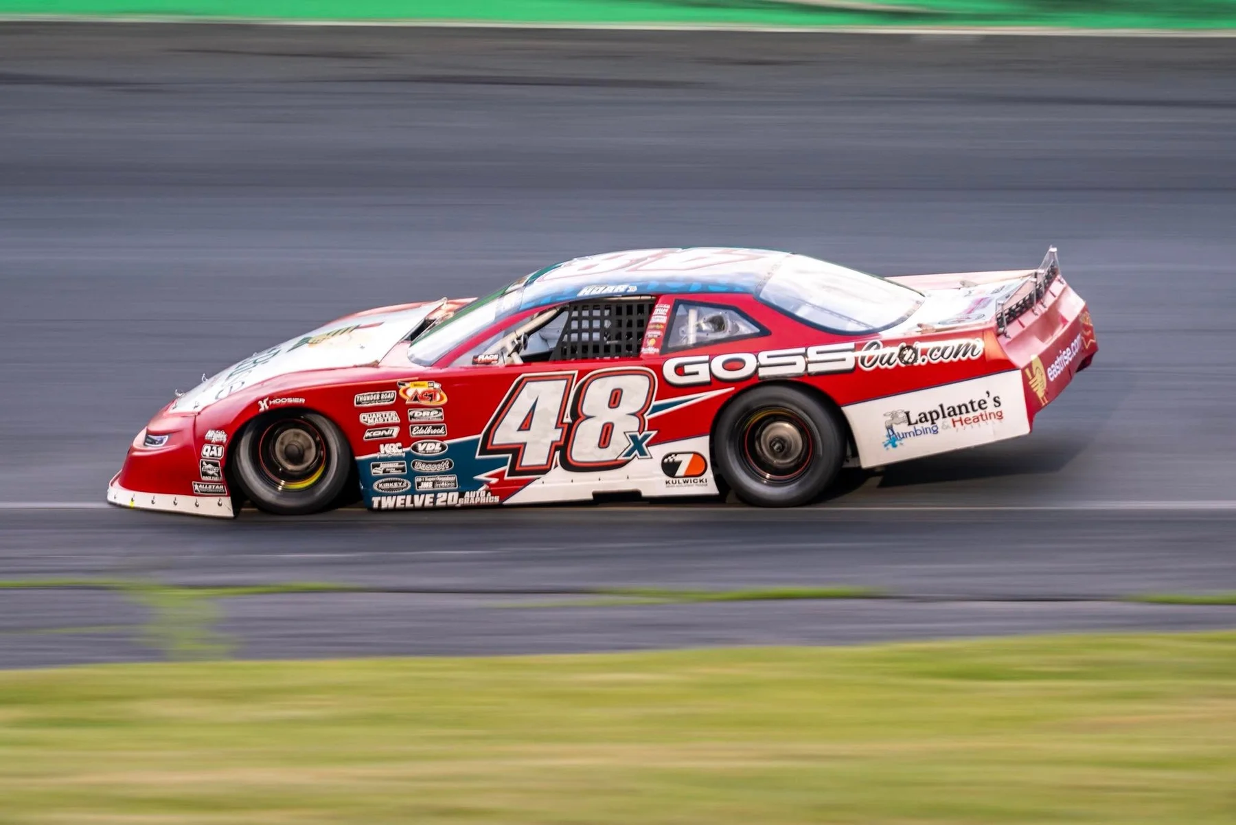 Taylor Hoar's red No. 48x stock car at speed on the Thunder Road asphalt, the background blurred with motion.
