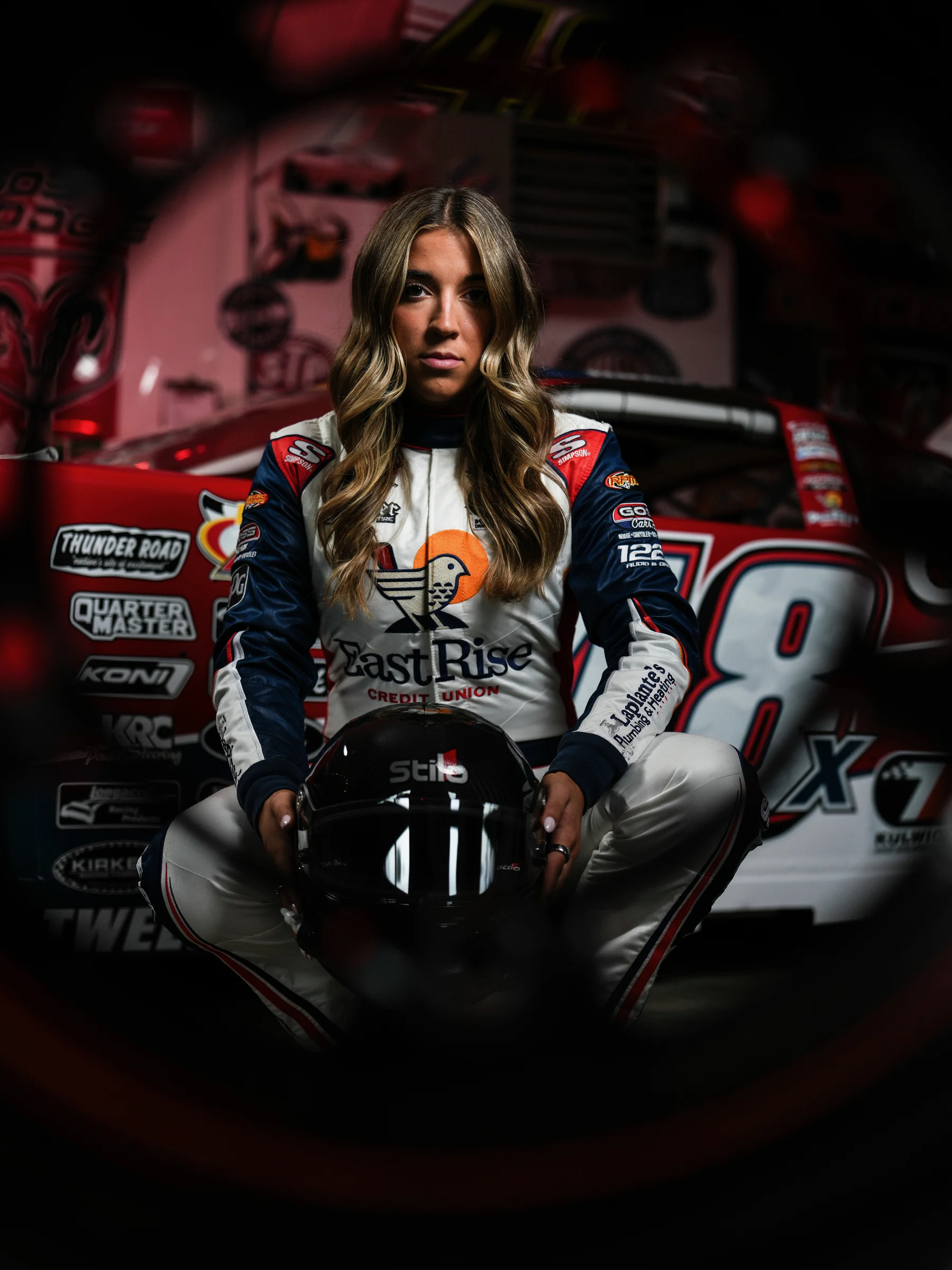 Taylor Hoar seated in her EastRise race suit, holding her helmet in front of the No. 48 car
