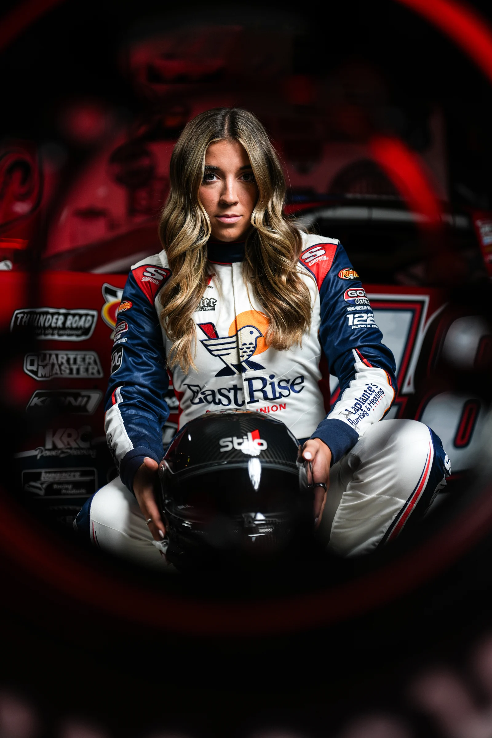 Taylor Hoar sits in front of the No. 48 car in her EastRise race suit, framed by a red roll cage.