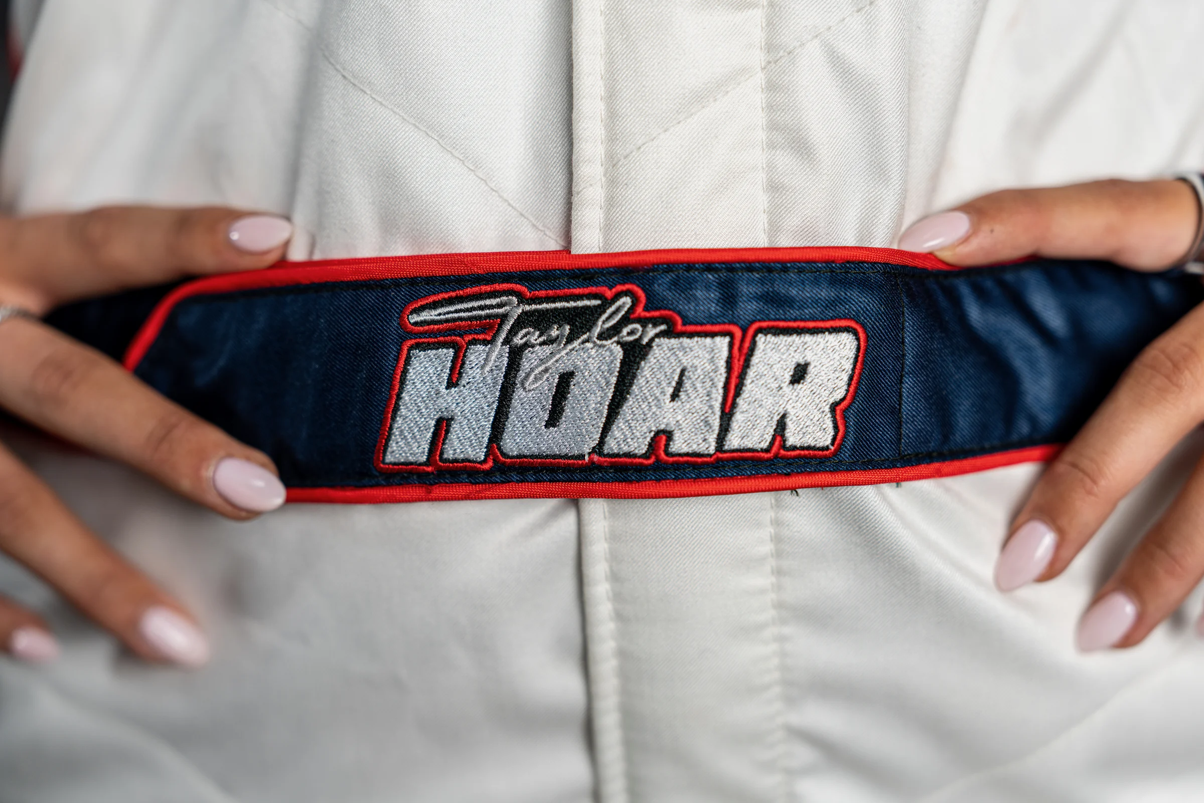 Close detail of Taylor Hoar holding the embroidered belt of her white race suit.