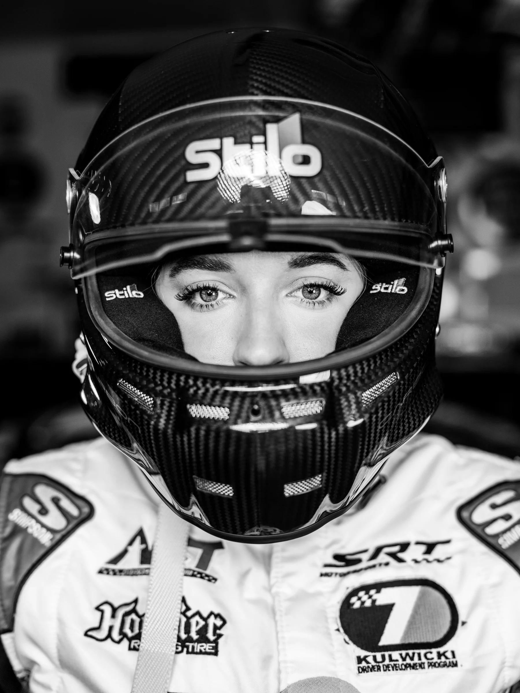 Black-and-white close portrait of Taylor Hoar looking through the visor of her racing helmet.