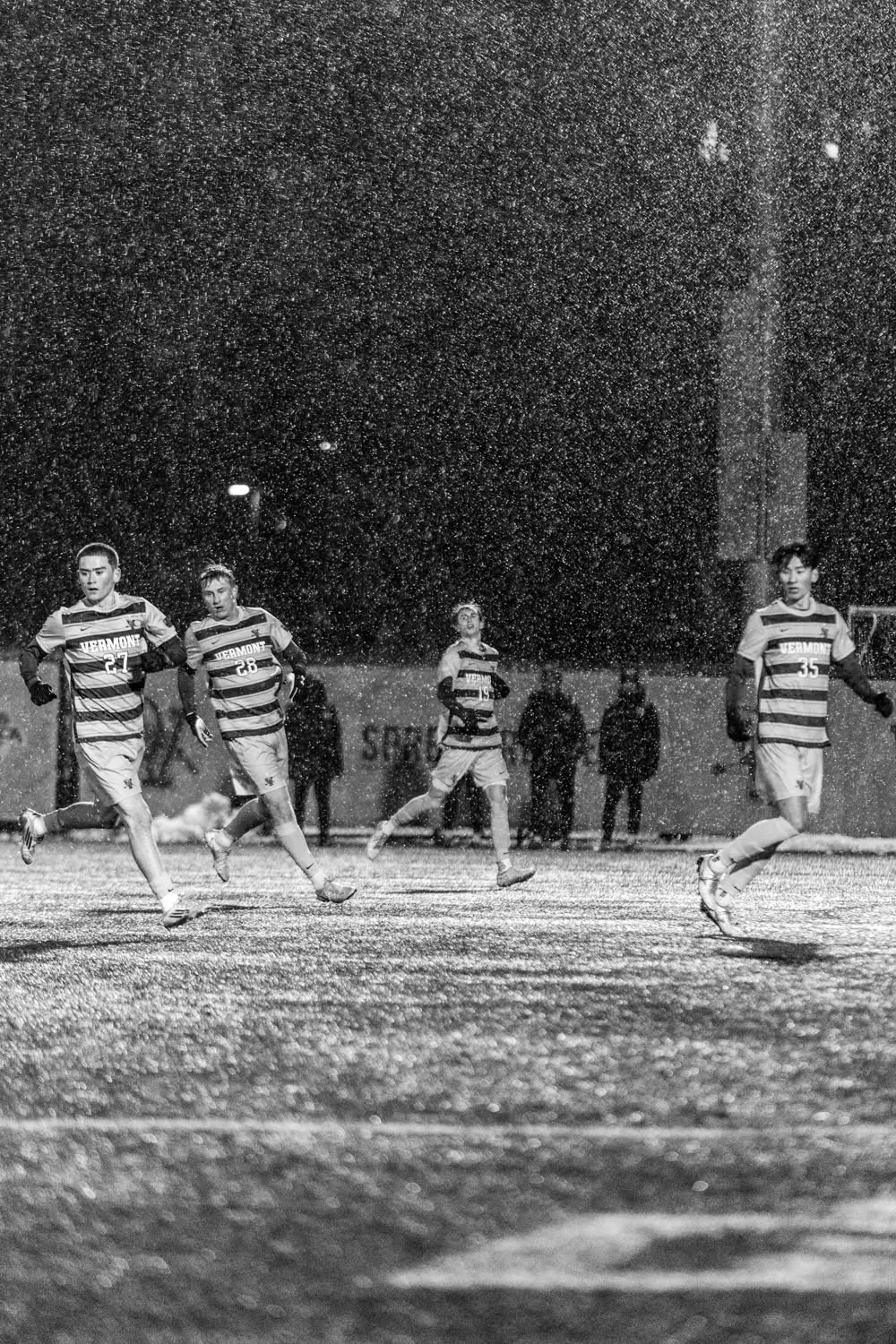 Soccer players contest the ball during a snowy night match at UVM.