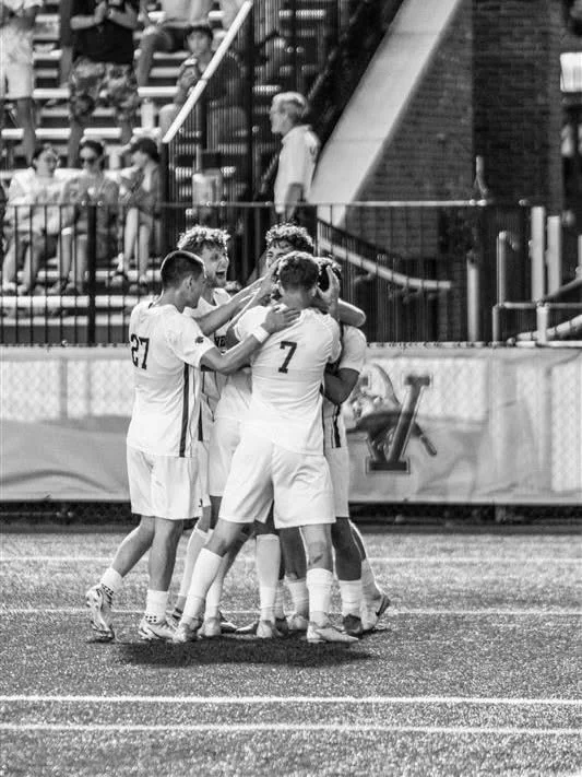 UVM men’s soccer players embrace near the goal after a play.