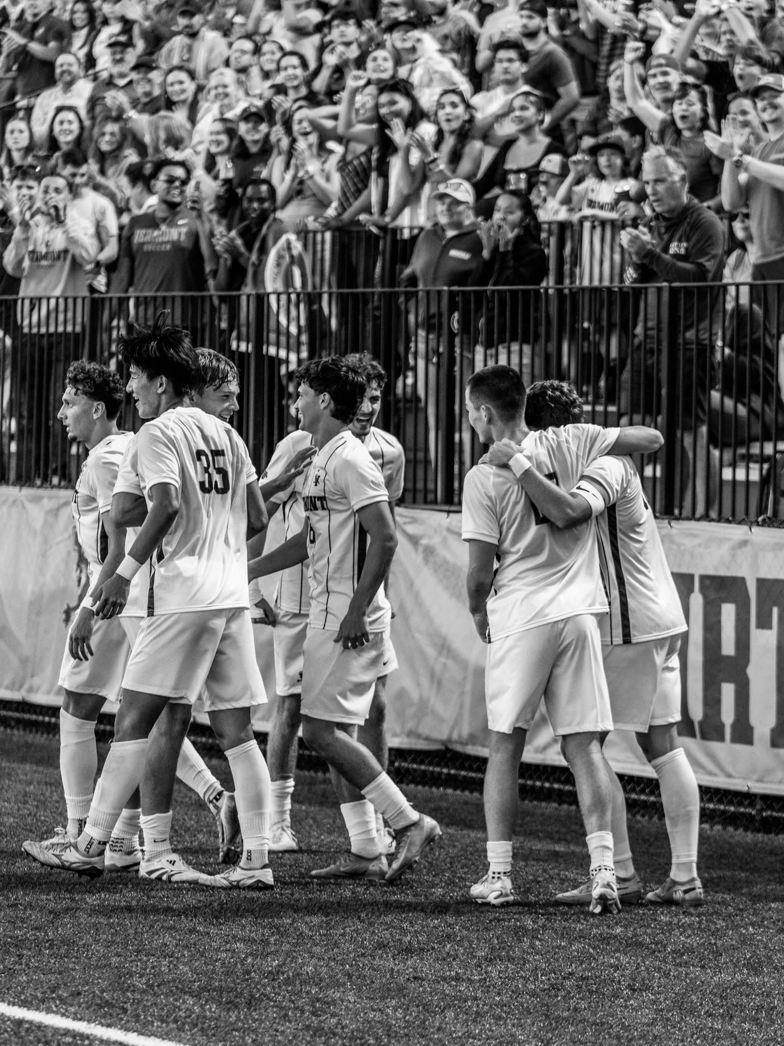 UVM men’s soccer players huddle in front of a cheering crowd.