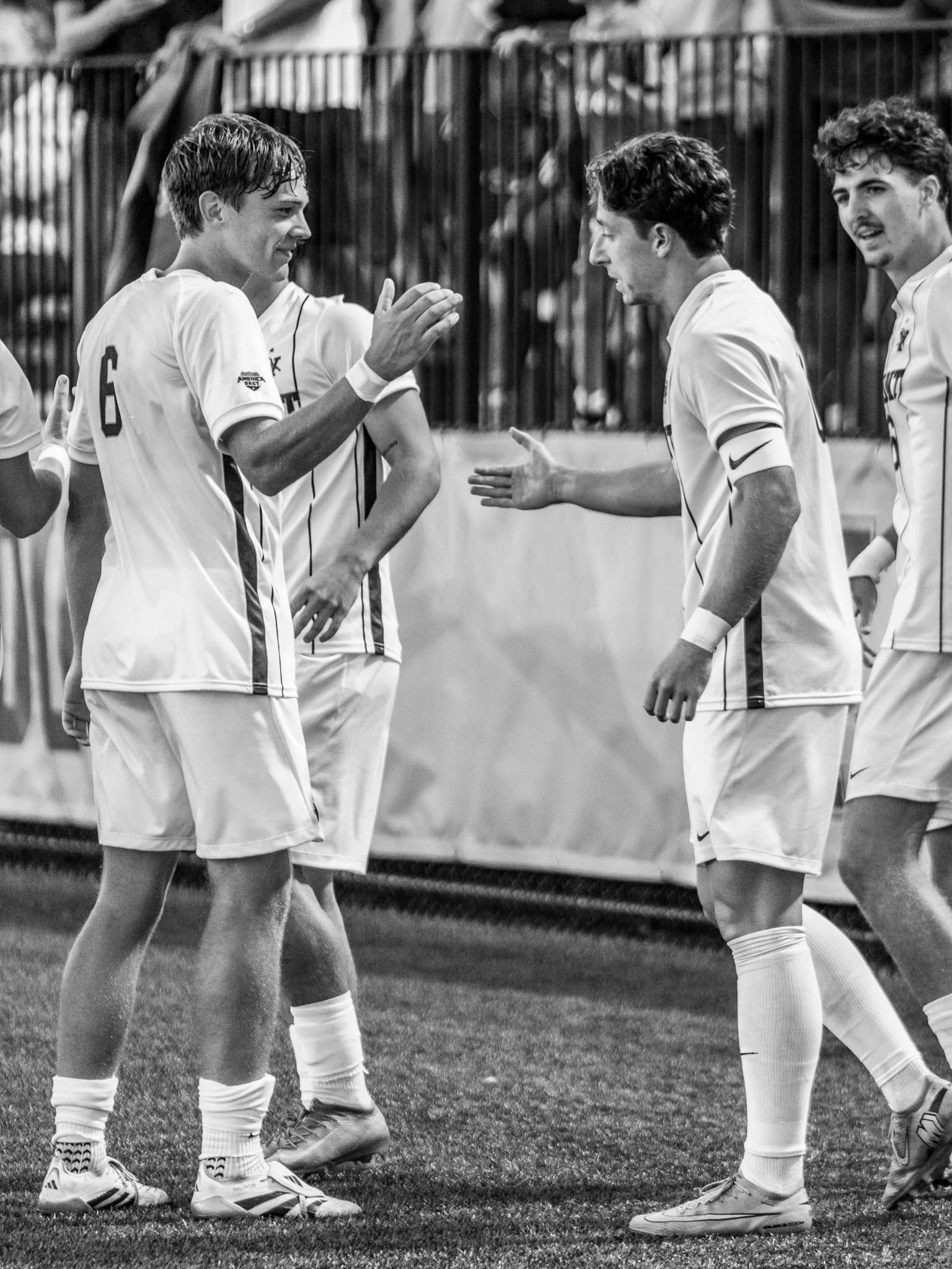 Three UVM men’s soccer players talk together on the field.