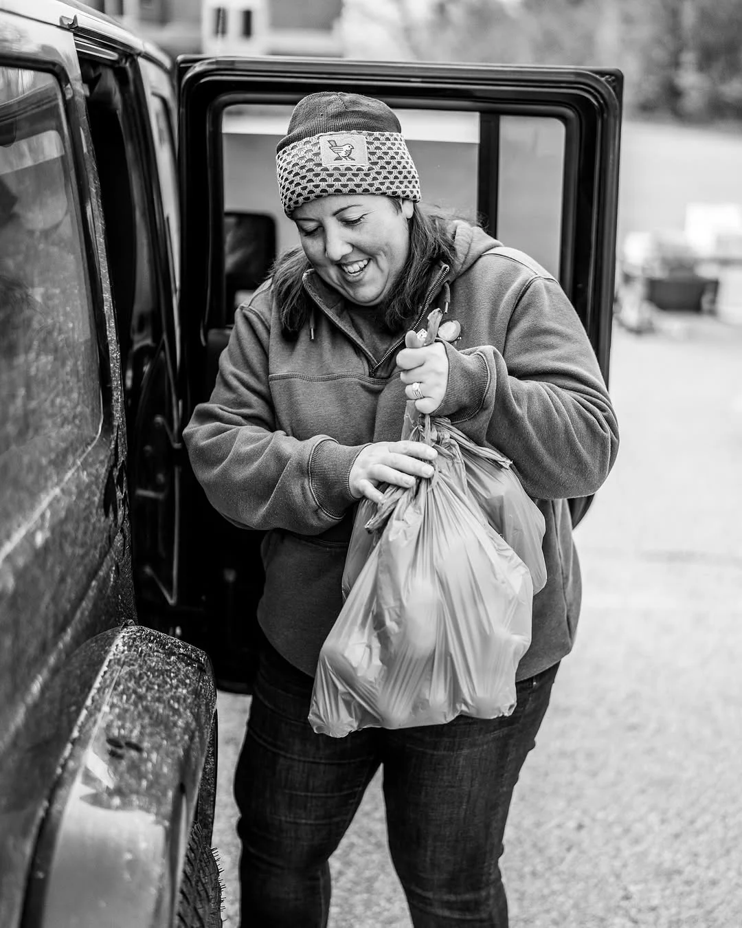 A volunteer carries a bag of produce from an open vehicle.
