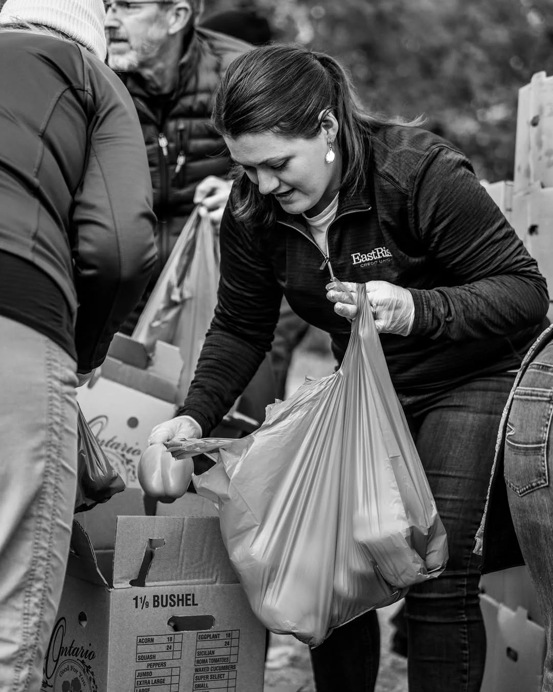 A volunteer lifts a bag of produce from a cardboard box.