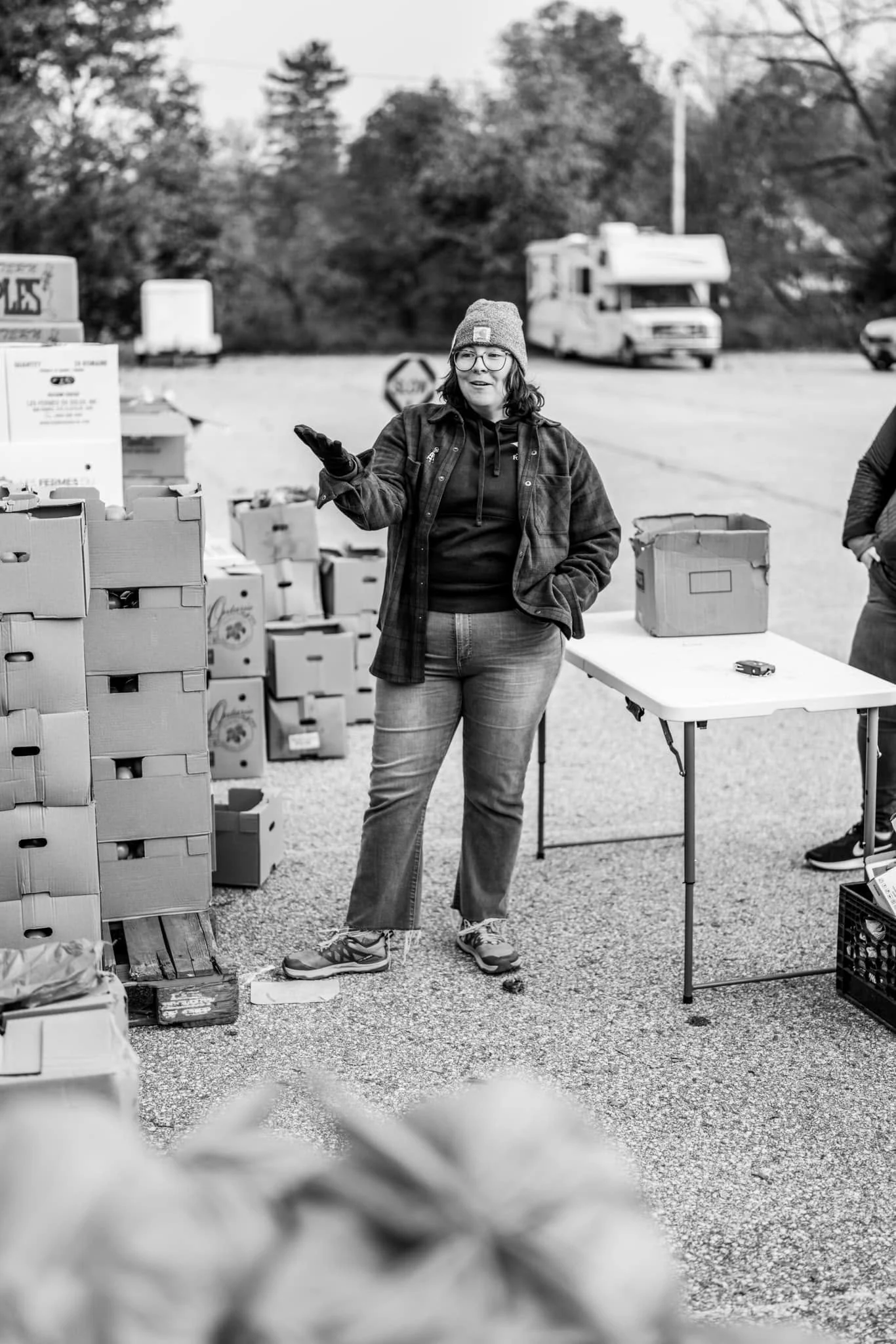 A volunteer stands beside stacked boxes of produce at a food distribution.