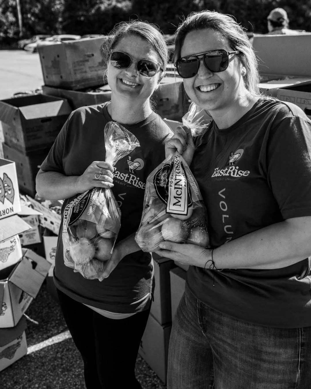 Two smiling volunteers hold bags of potatoes and carrots.