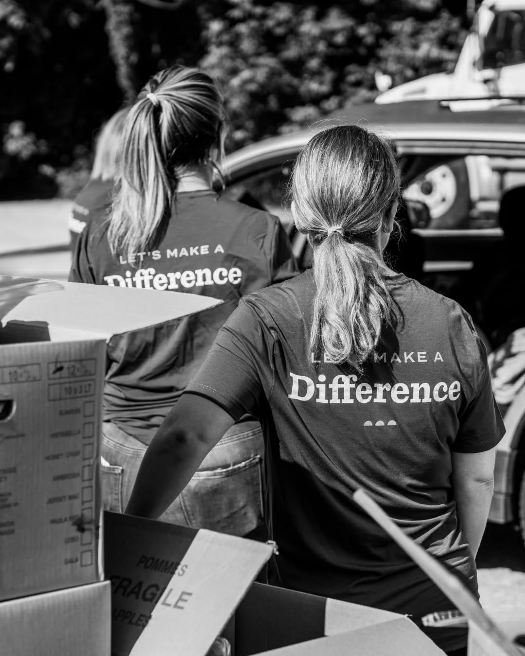 Volunteers sort produce boxes beside a parked vehicle.