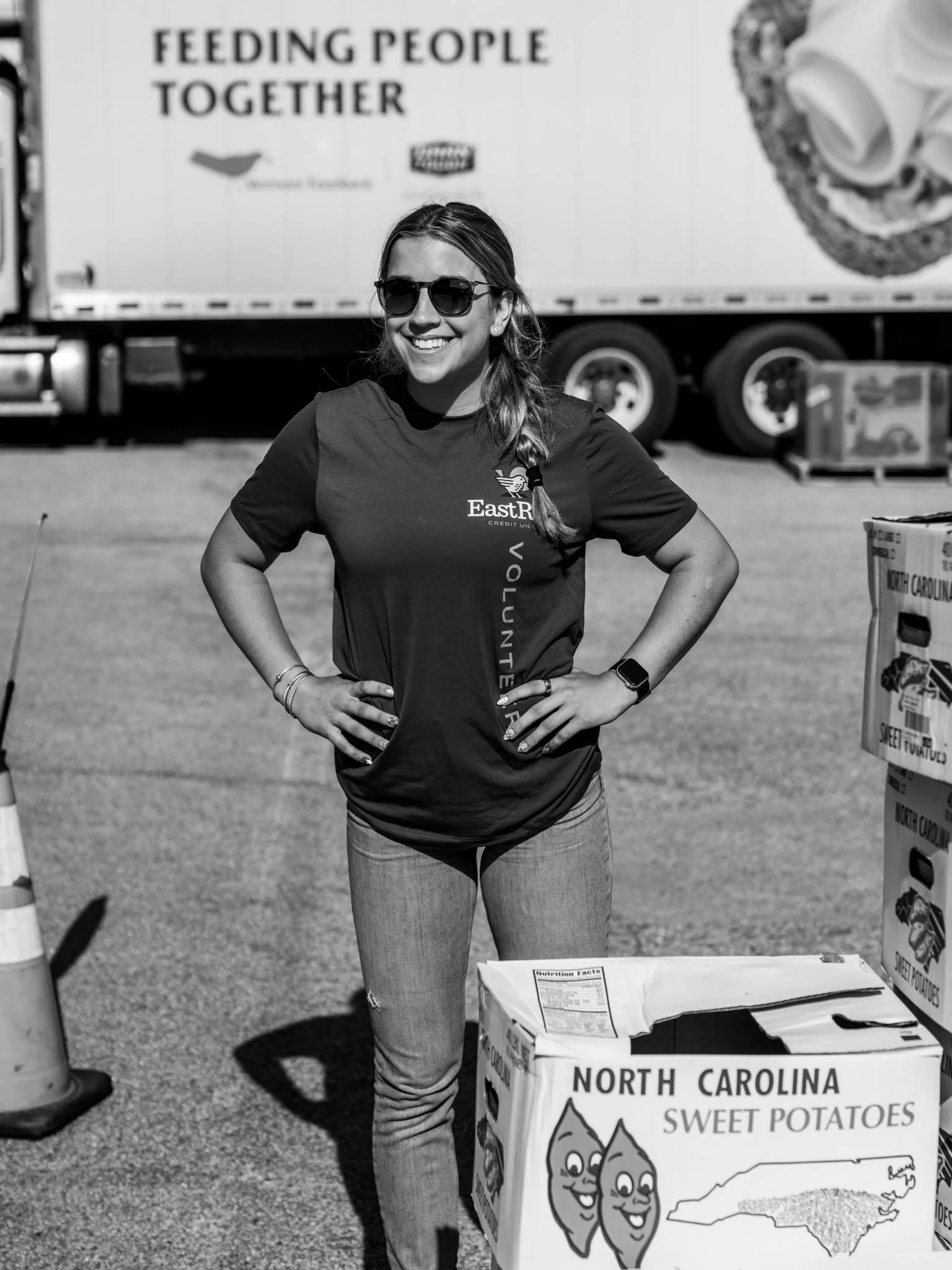 A volunteer stands with her hands on her hips beside a VeggieVanGo truck and distribution sign.
